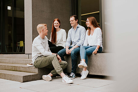 Eine Gruppe mit vier Auszubildenden sitzt gemeinsam im Außenbereich des Ernsting's family Campus.